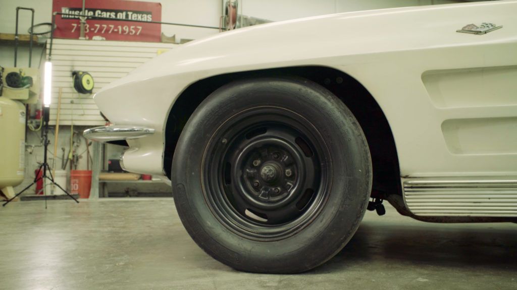 White classic car's front wheel, black tire, in a garage.