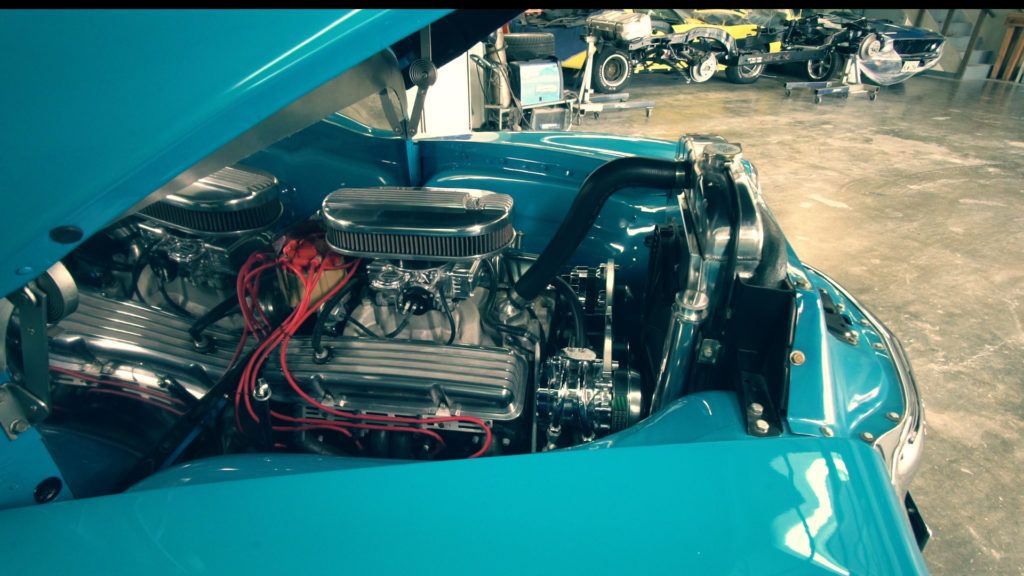 Blue classic car engine bay, open hood, chrome components, red wires, interior shop.