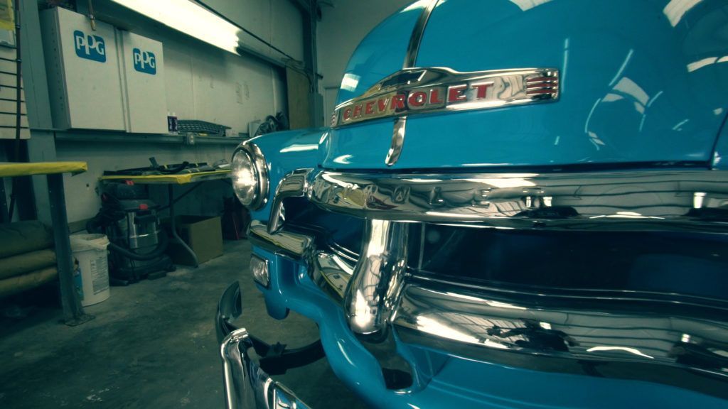 Blue classic Chevrolet car in a garage, chrome details shine, hood open.