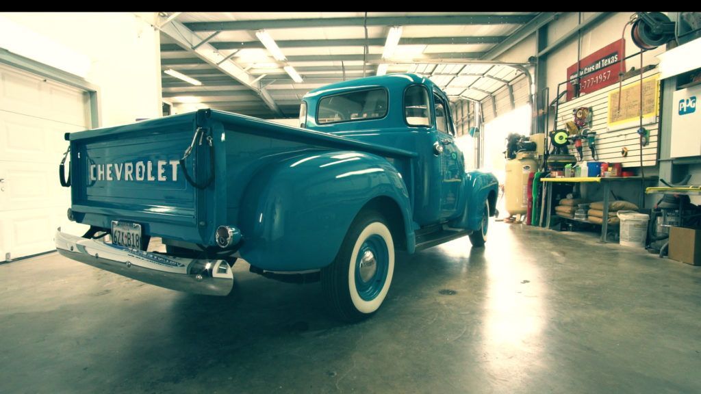Teal vintage Chevrolet truck inside a garage with tools and open bay door.