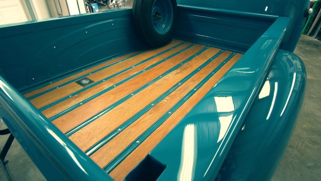 Teal truck bed with wooden slats, spare tire, and metal strips.