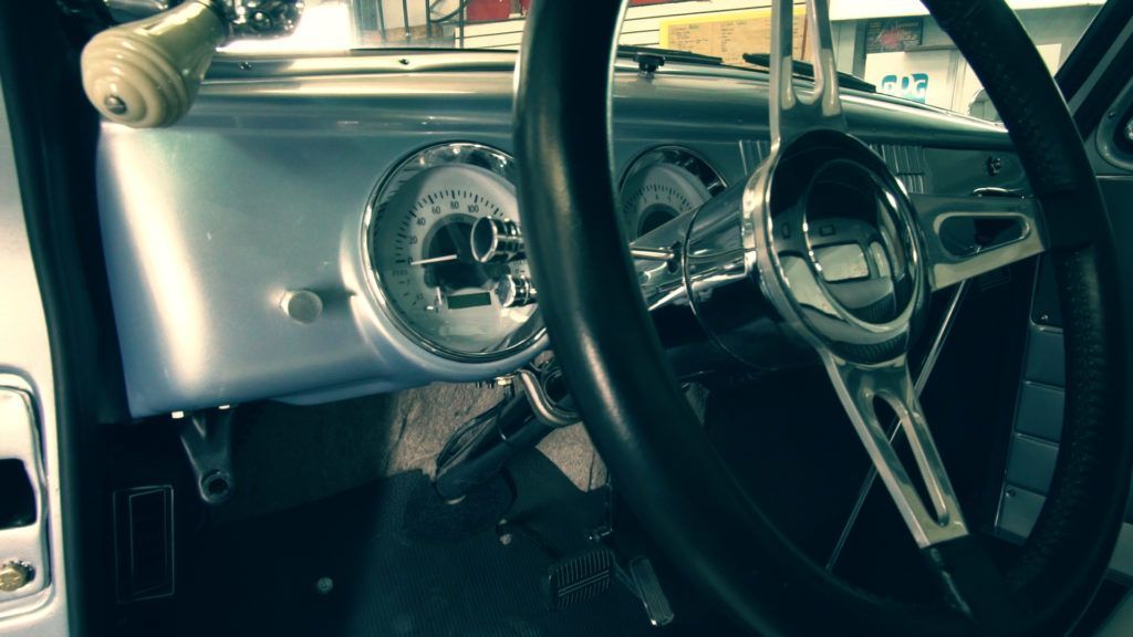 Interior of classic car with silver dash and chrome steering wheel.