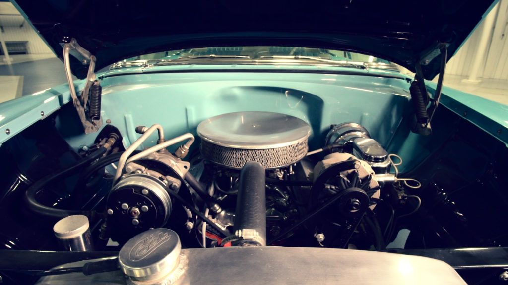 Open hood of a teal classic car, showcasing a detailed engine bay.