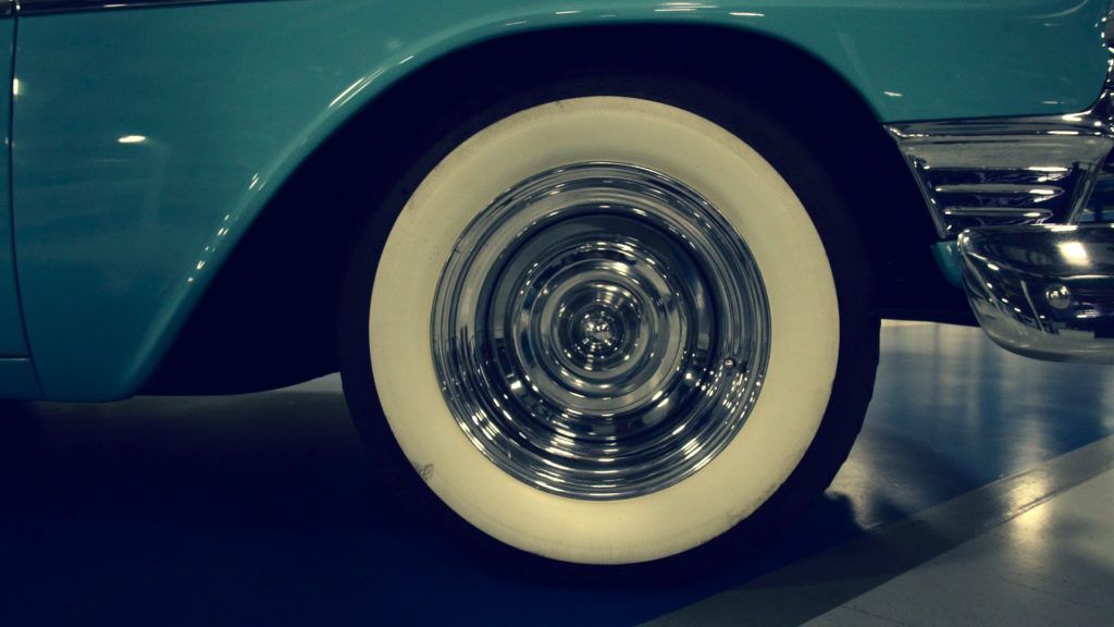 Close-up of a vintage turquoise car's tire with a white sidewall and chrome hubcap.