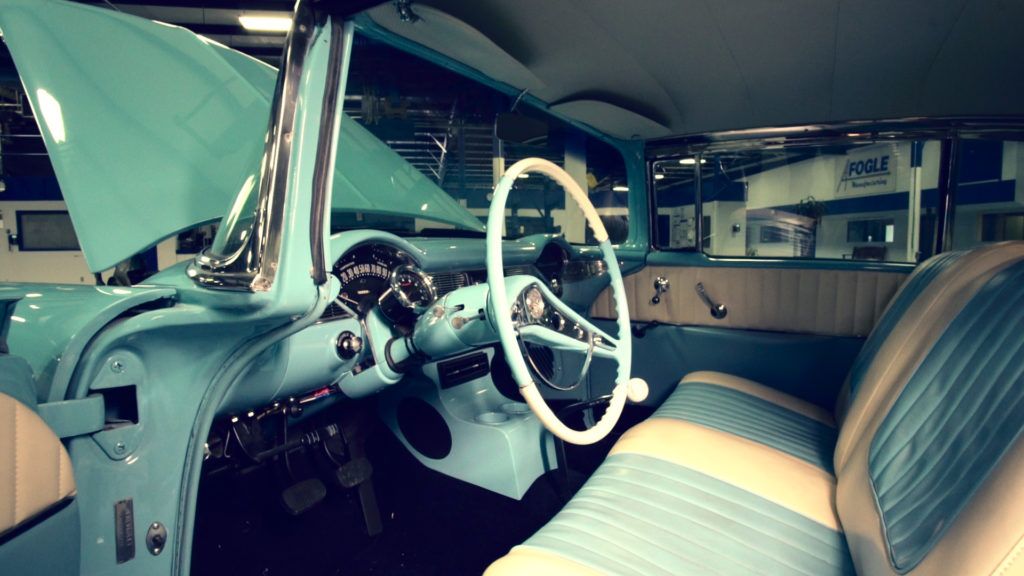 Inside of a vintage turquoise car with a white steering wheel, interior light blue.