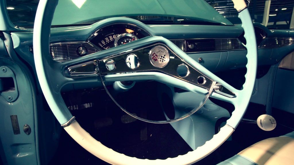 Teal and white classic car interior: dashboard, steering wheel, and gauges.