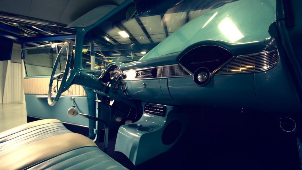 Interior of a teal classic car. Dashboard, steering wheel, and seats in view.