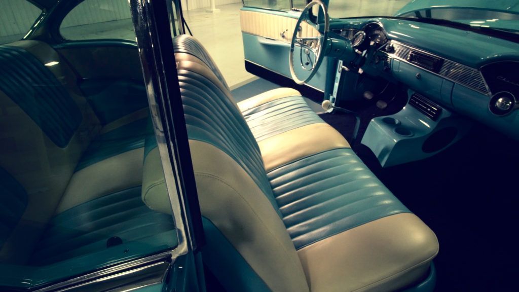 Interior of a classic blue and cream car, featuring front and back bench seats, dashboard, and steering wheel.