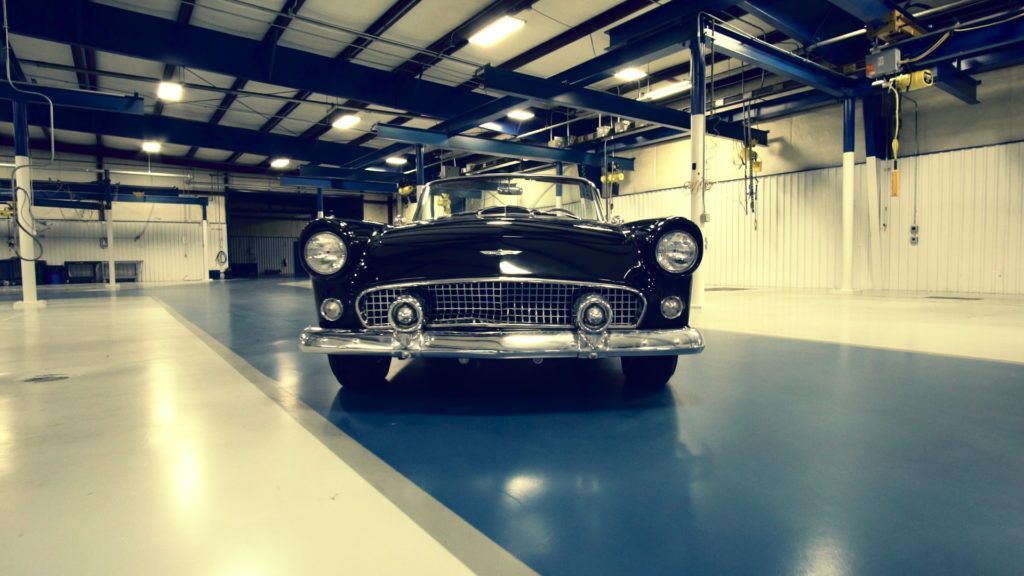 Black vintage car parked in an empty industrial warehouse. Chrome details, shiny floor.