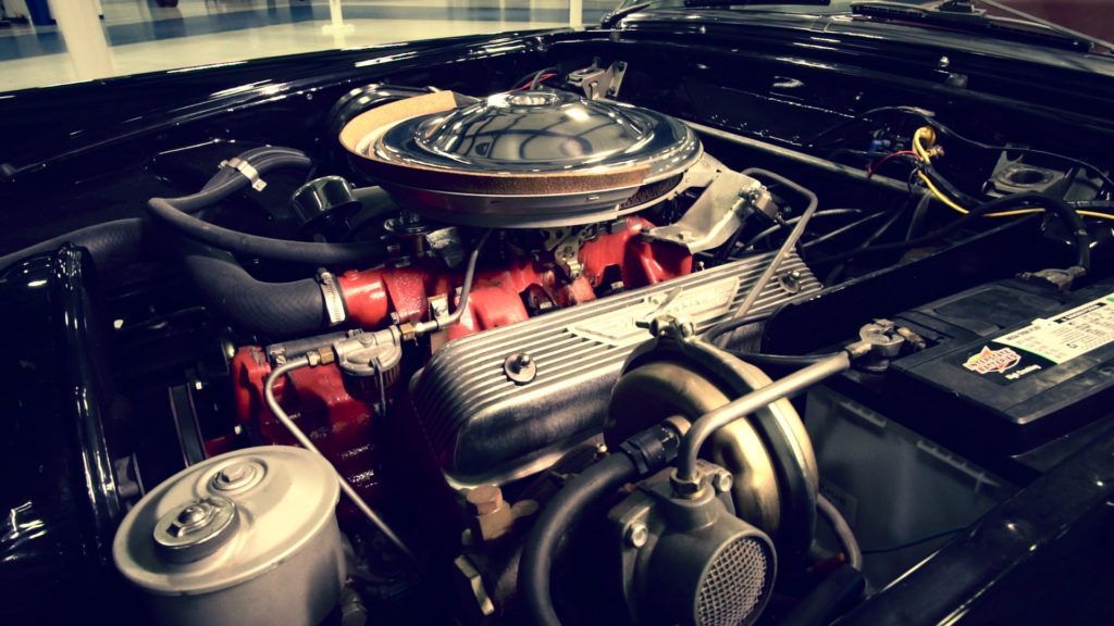 Black vintage car engine, chrome air cleaner, red engine block, and battery visible.