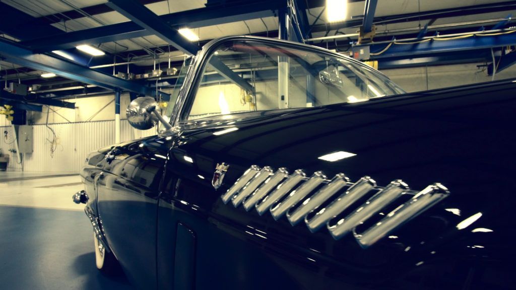 Black classic car, partially visible in a garage, displaying chrome side vents and mirror.
