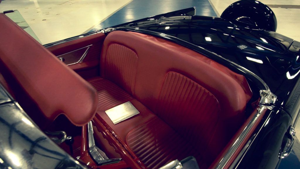 Red interior of a black classic convertible car, with a shiny exterior and red seats.