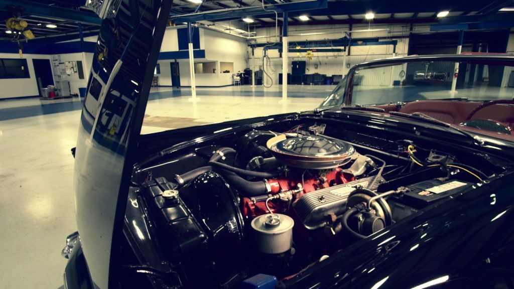 Black classic car with hood open, engine visible in a well-lit garage.