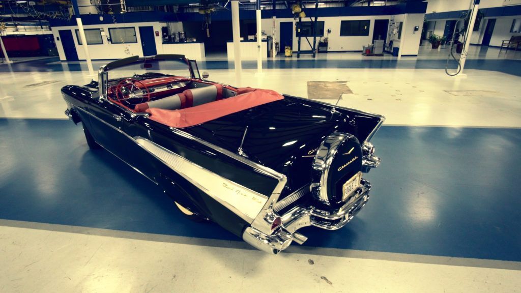 Black convertible car with chrome details, red interior, parked inside a large garage.