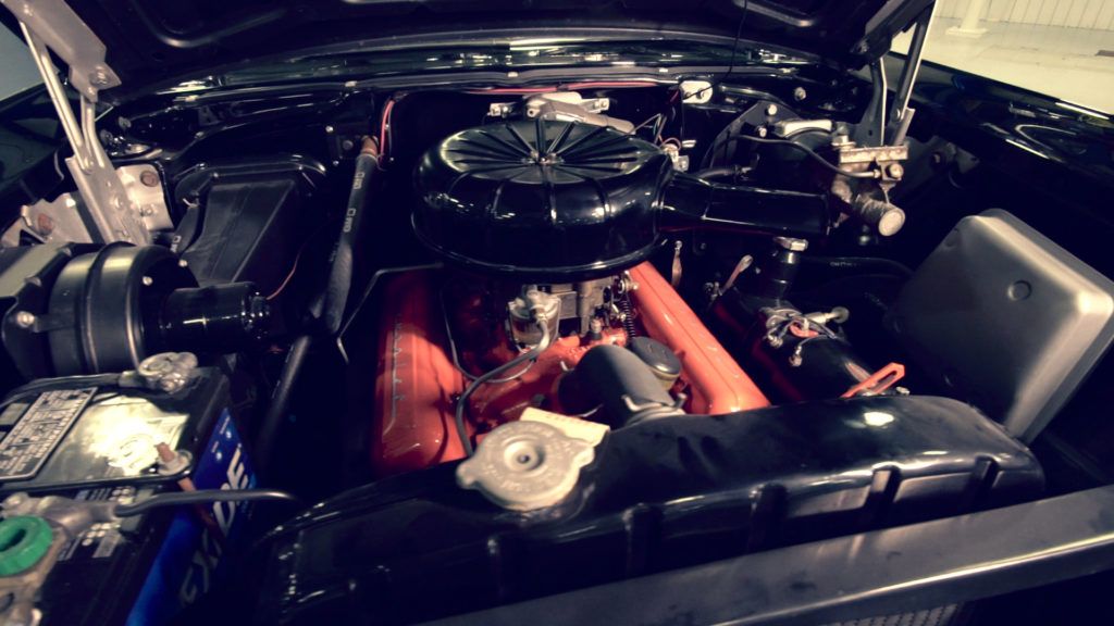 Black classic car engine bay, red engine components, black air filter, silver radiator, setting dark.