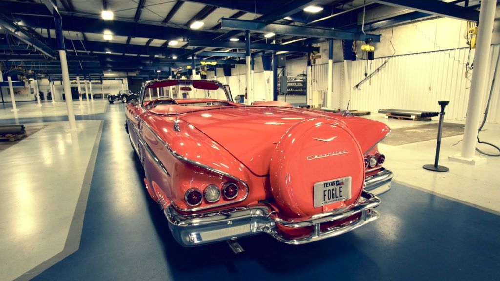 Red classic convertible car parked inside a large, brightly lit garage.