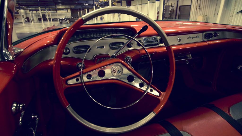Red dashboard of a classic Chevrolet, steering wheel in focus. Silver accents, retro design.