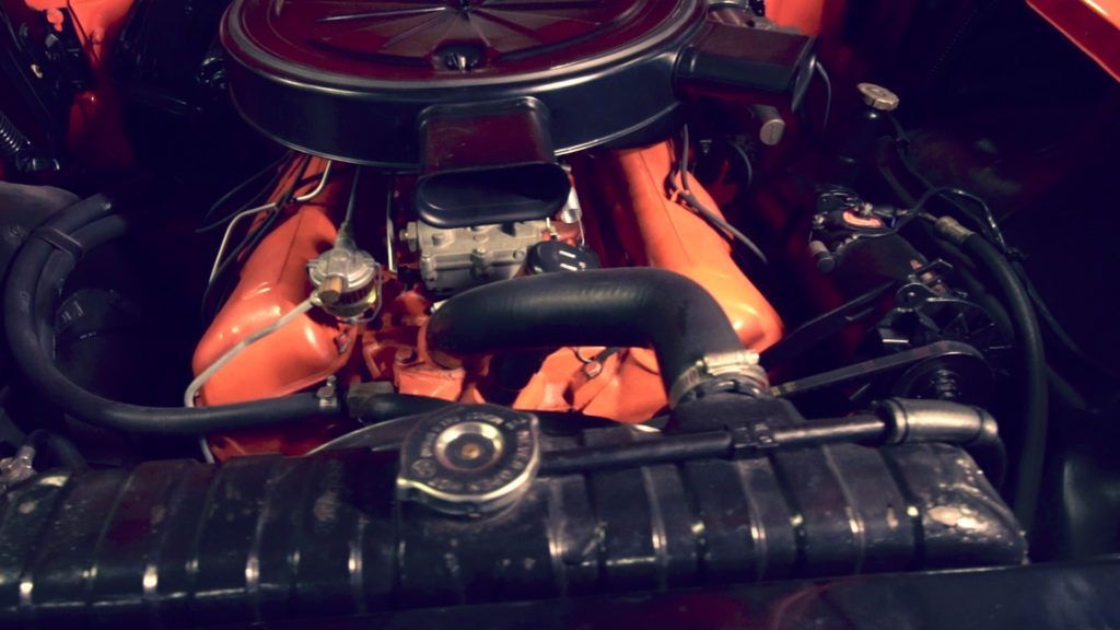 Orange classic car engine with black intake and radiator.