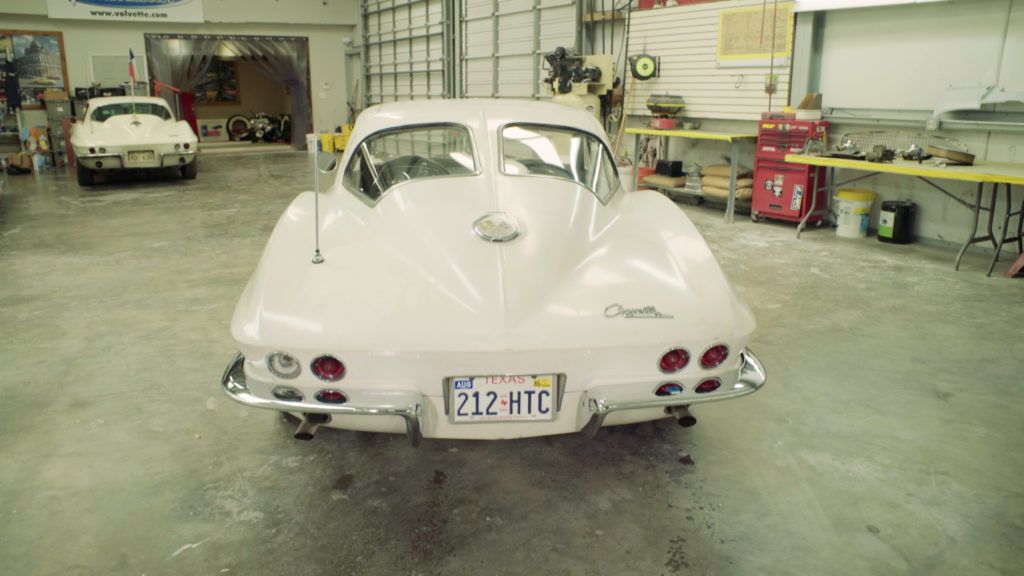 White classic Corvette coupe in a garage, with license plate 212-HTC. Another Corvette in the background.