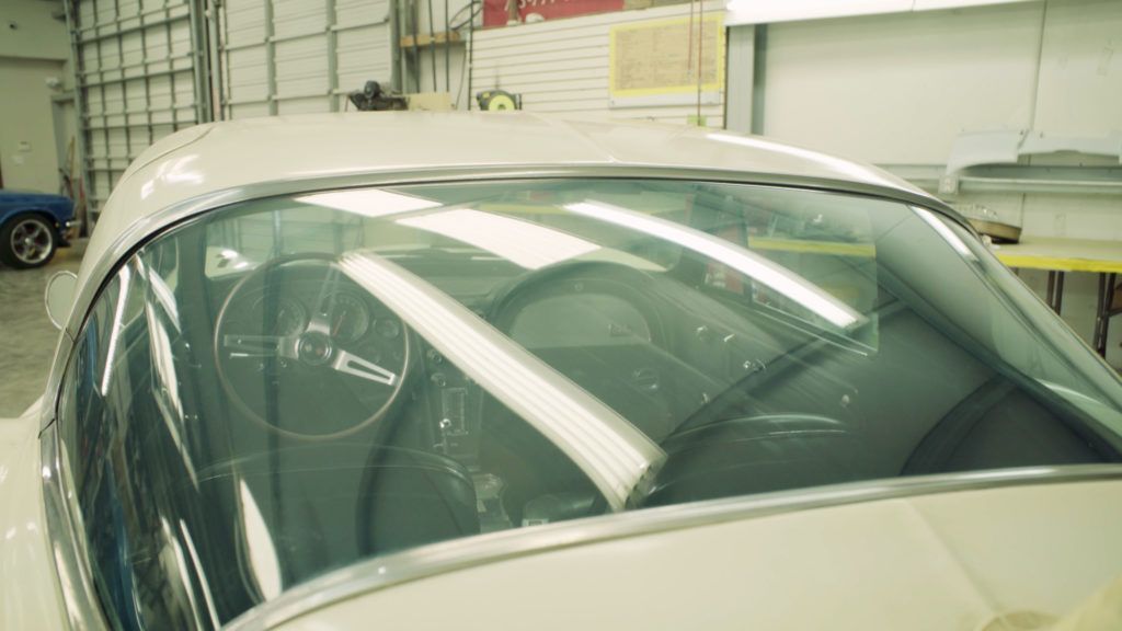 White car's interior visible through the windshield. Steering wheel, dashboard, and seats are in view.