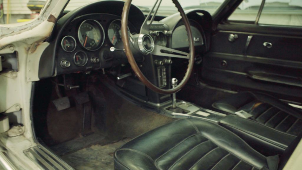 Interior of a classic black and white car with gauges, wooden steering wheel, and black leather seats.
