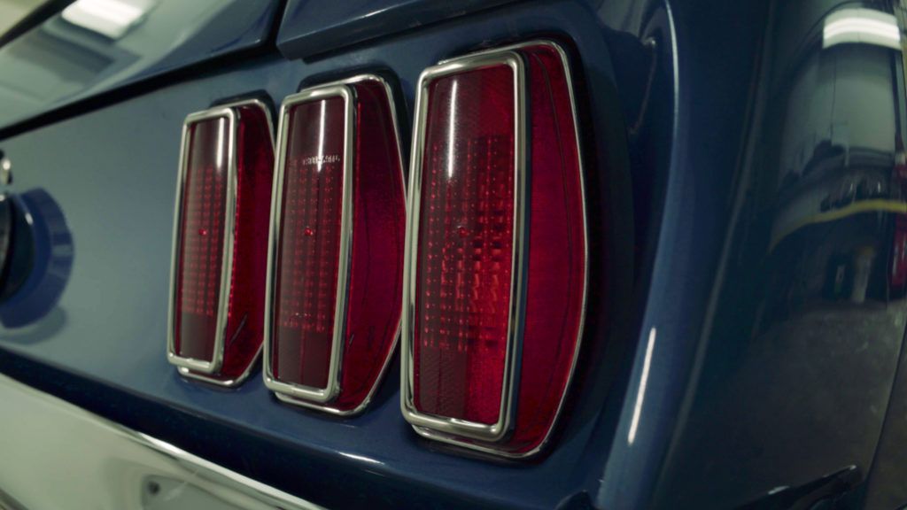 Close-up of a blue classic car's rear with three red tail lights trimmed in chrome.
