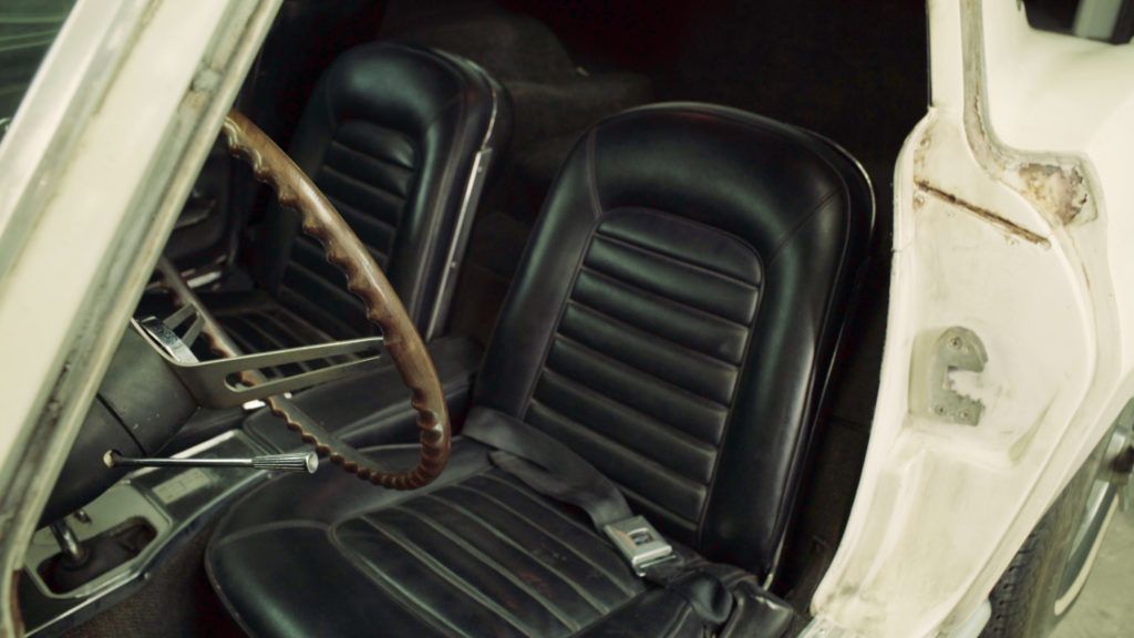 Interior view of a classic car with black leather seats, steering wheel, and visible door.