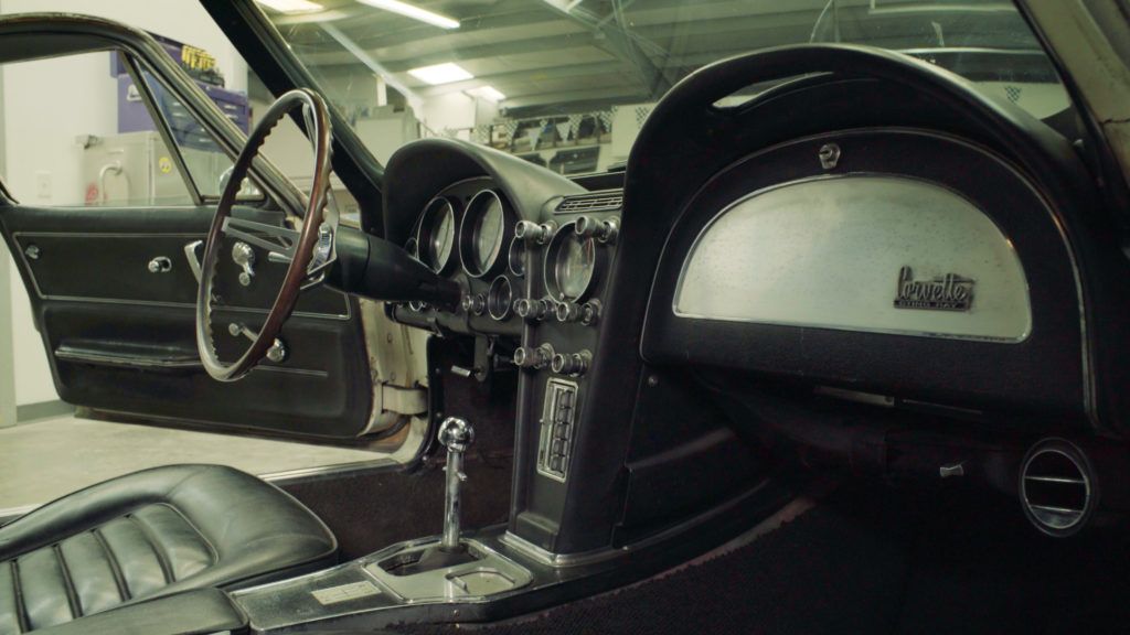 Interior of a classic black Corvette, featuring the dashboard, steering wheel, and seats.