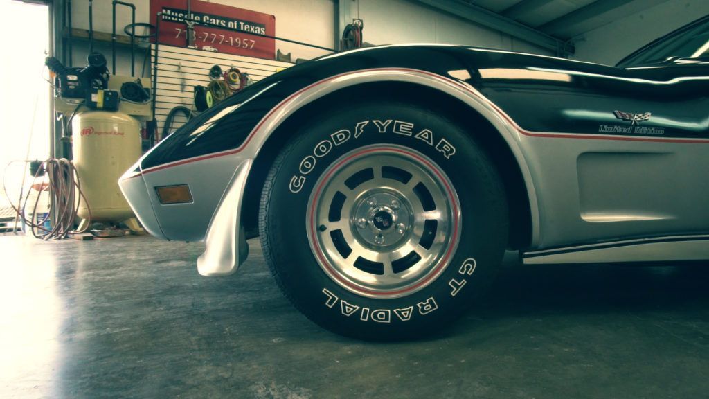 Black and silver Corvette's front tire in a garage; Goodyear Radial GT tire, alloy wheel, and silver trim.