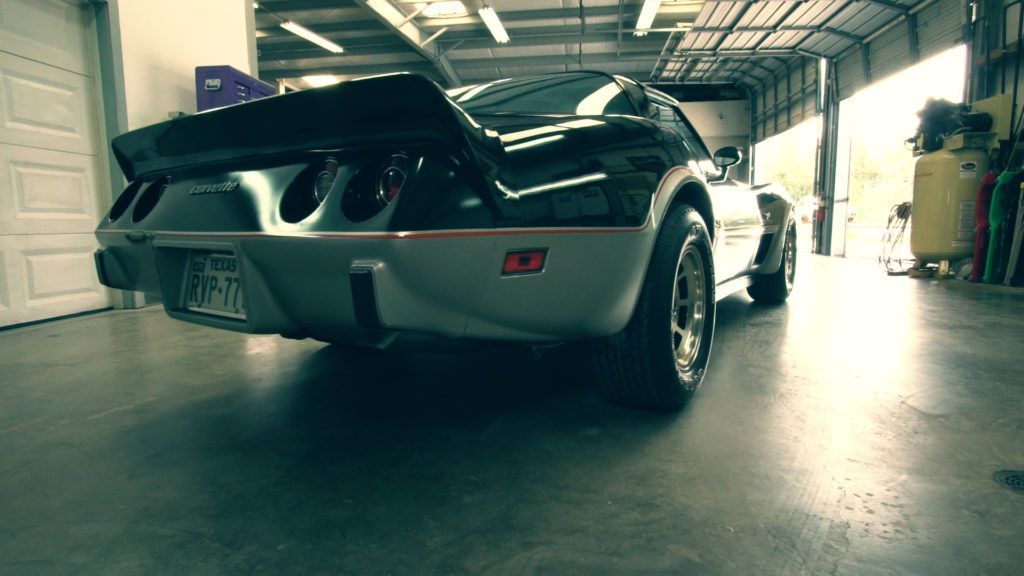 Black and silver Corvette in a garage with the garage door open.