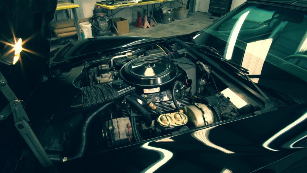 Black Corvette with hood open, revealing engine, in a garage.