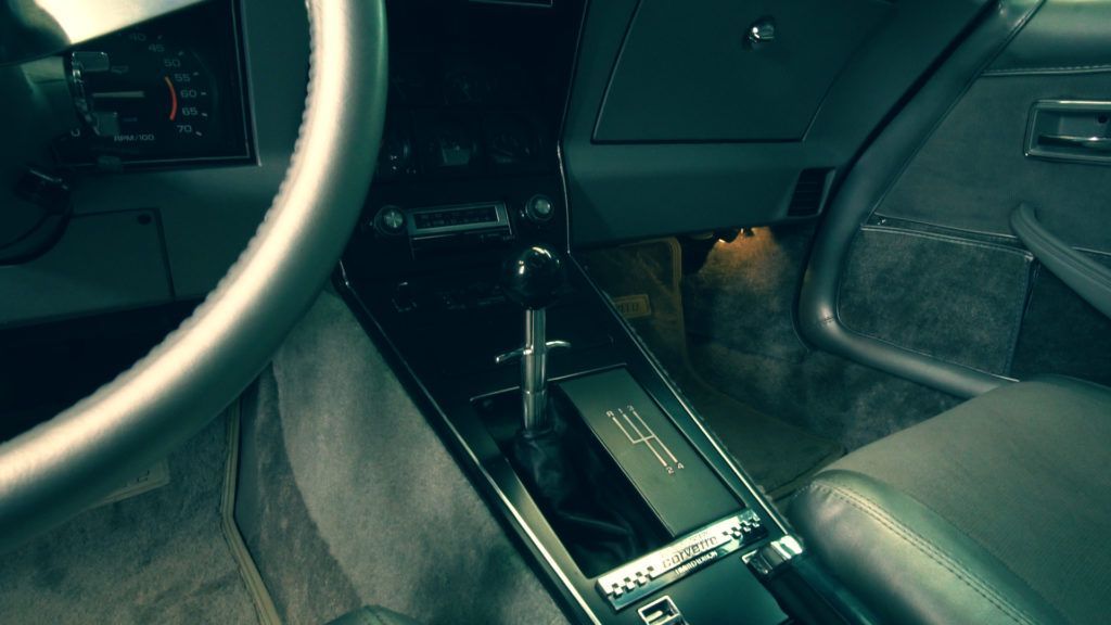 Interior of a classic car, focus on the gear shift, dashboard, and steering wheel. Dark colors.