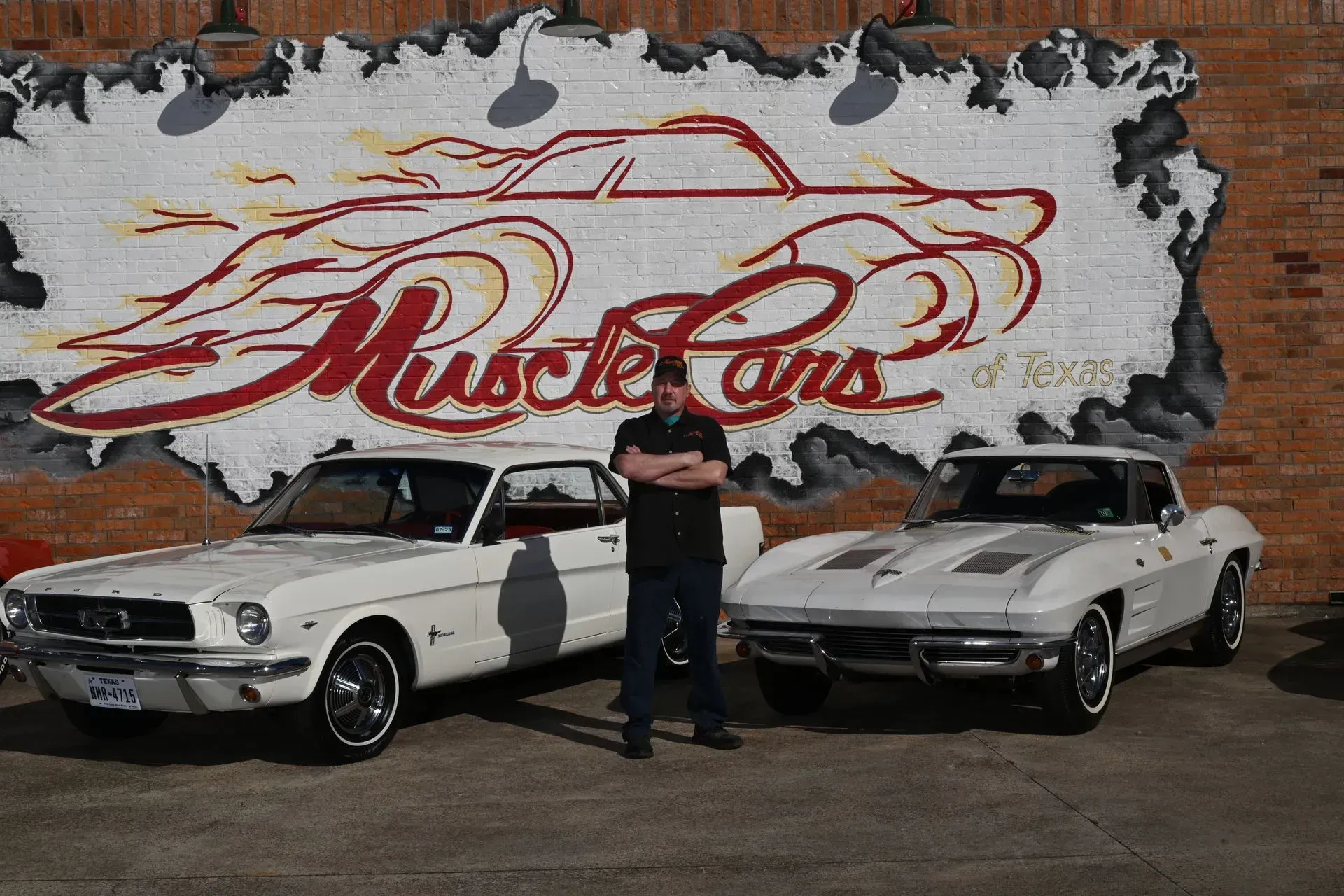 Man standing between two white classic muscle cars in front of a 