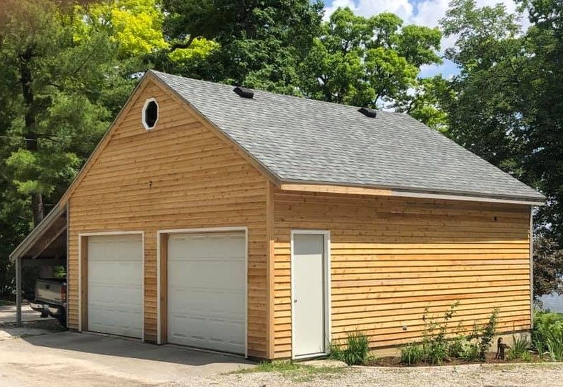 A wooden garage with two garage doors and a gray roof.