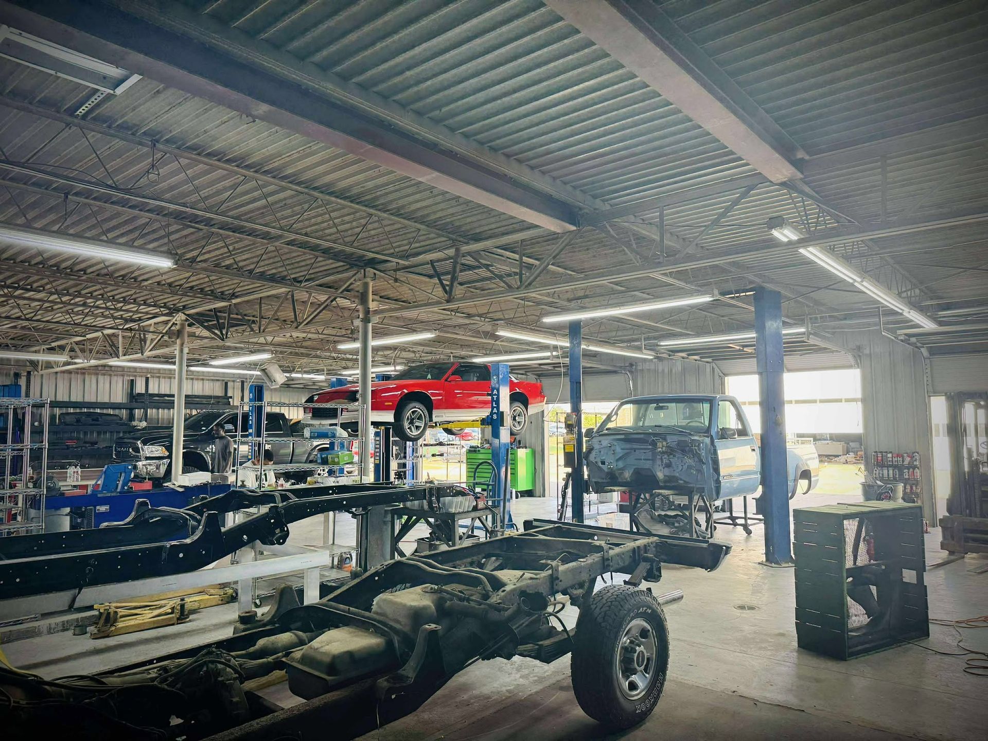 Inside a large auto repair shop, a red car and a blue truck are elevated.