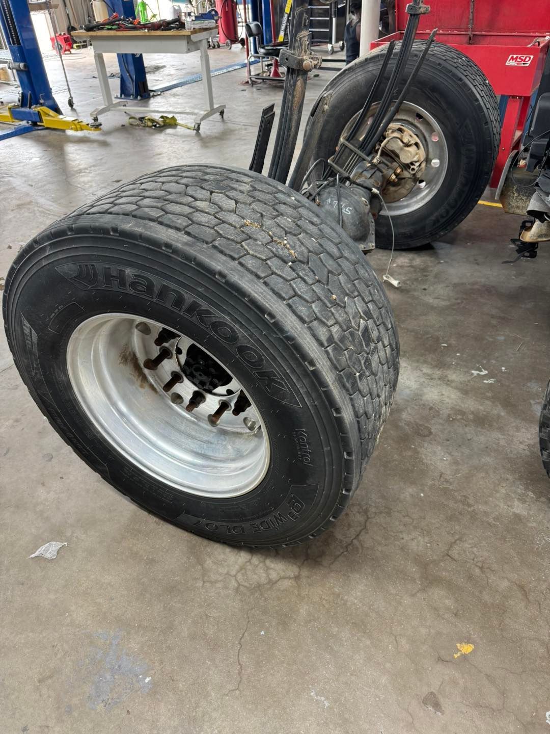 Pair of large truck tires on an axle in a garage.