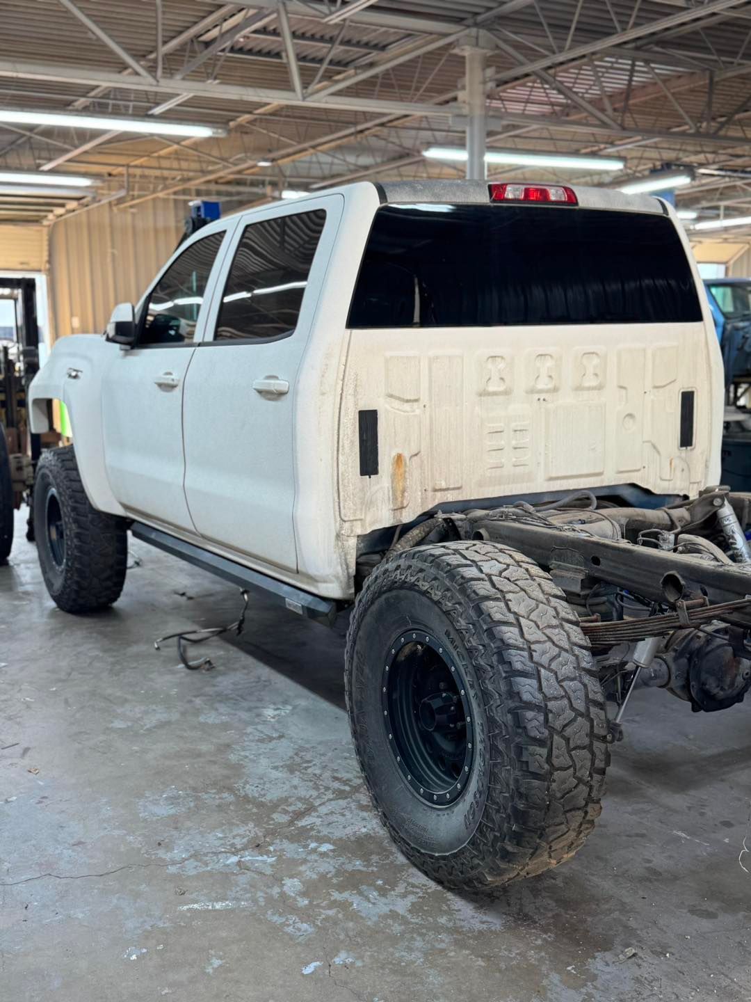 White pickup truck undergoing repairs in a garage; body removed, tires visible.