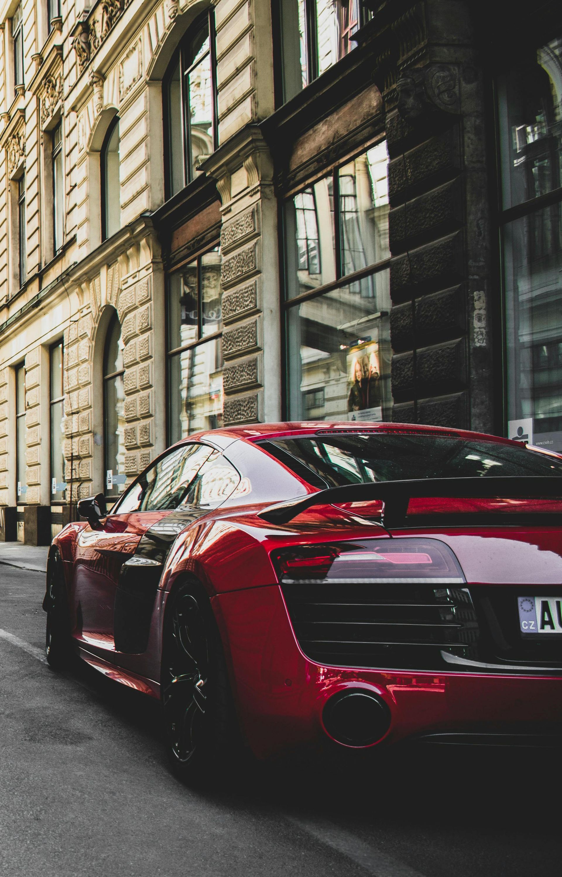 Red sports car parked on a narrow street in front of an old building with windows and columns.