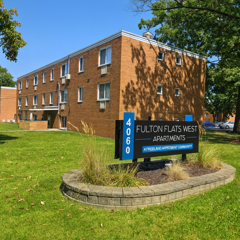 Fulton Flats West Apartments building with sign on a grassy lawn. Brick exterior, blue sign.