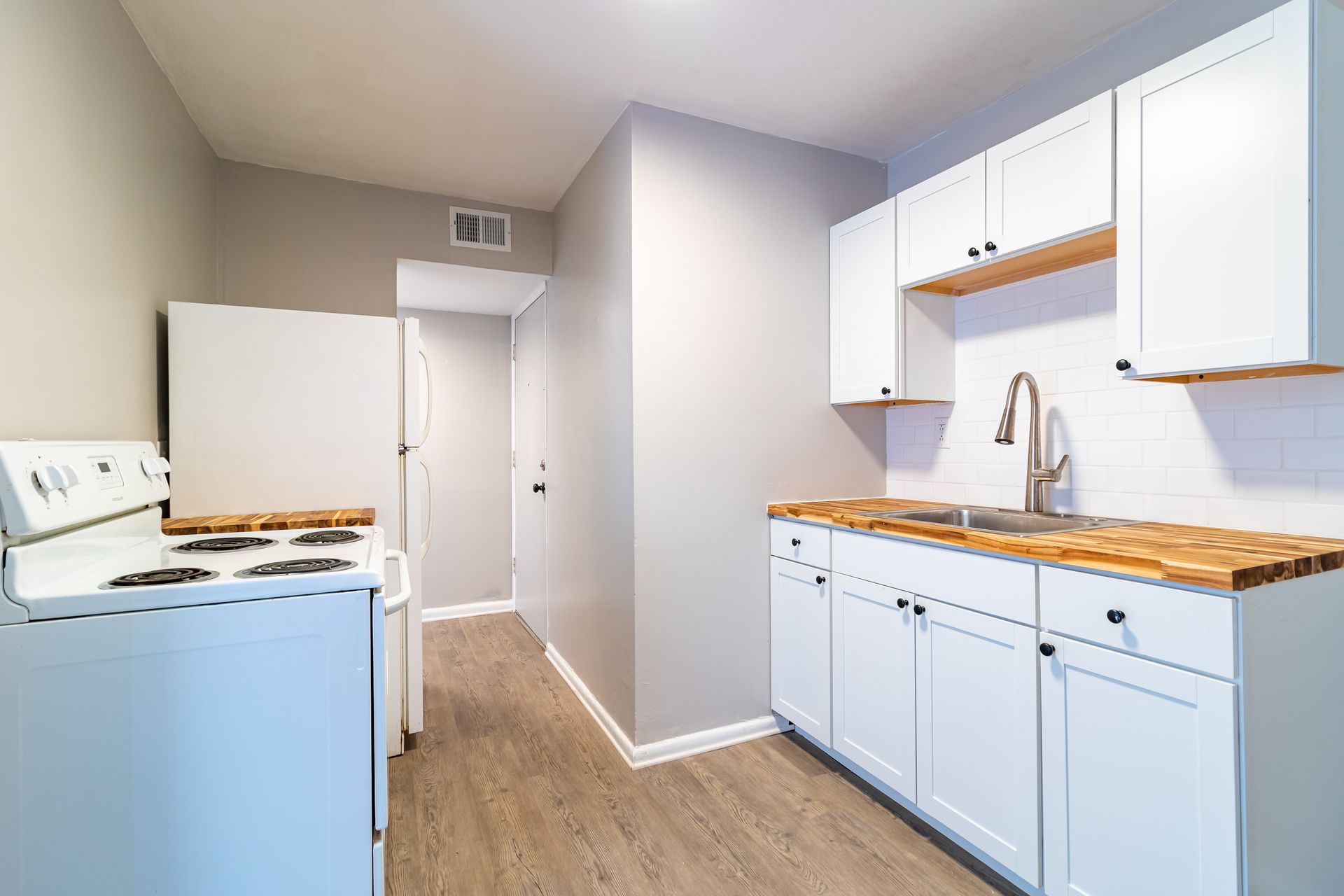 White kitchen with wood countertops, white cabinets, and appliances, in a small space.
