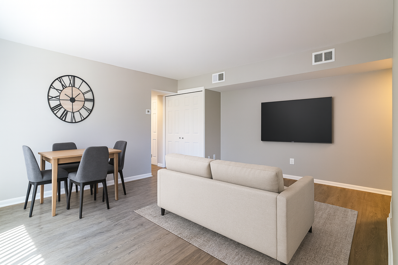 Living room with dining table, sofa, TV, and a large clock. Gray walls, wood floor, and neutral colors.