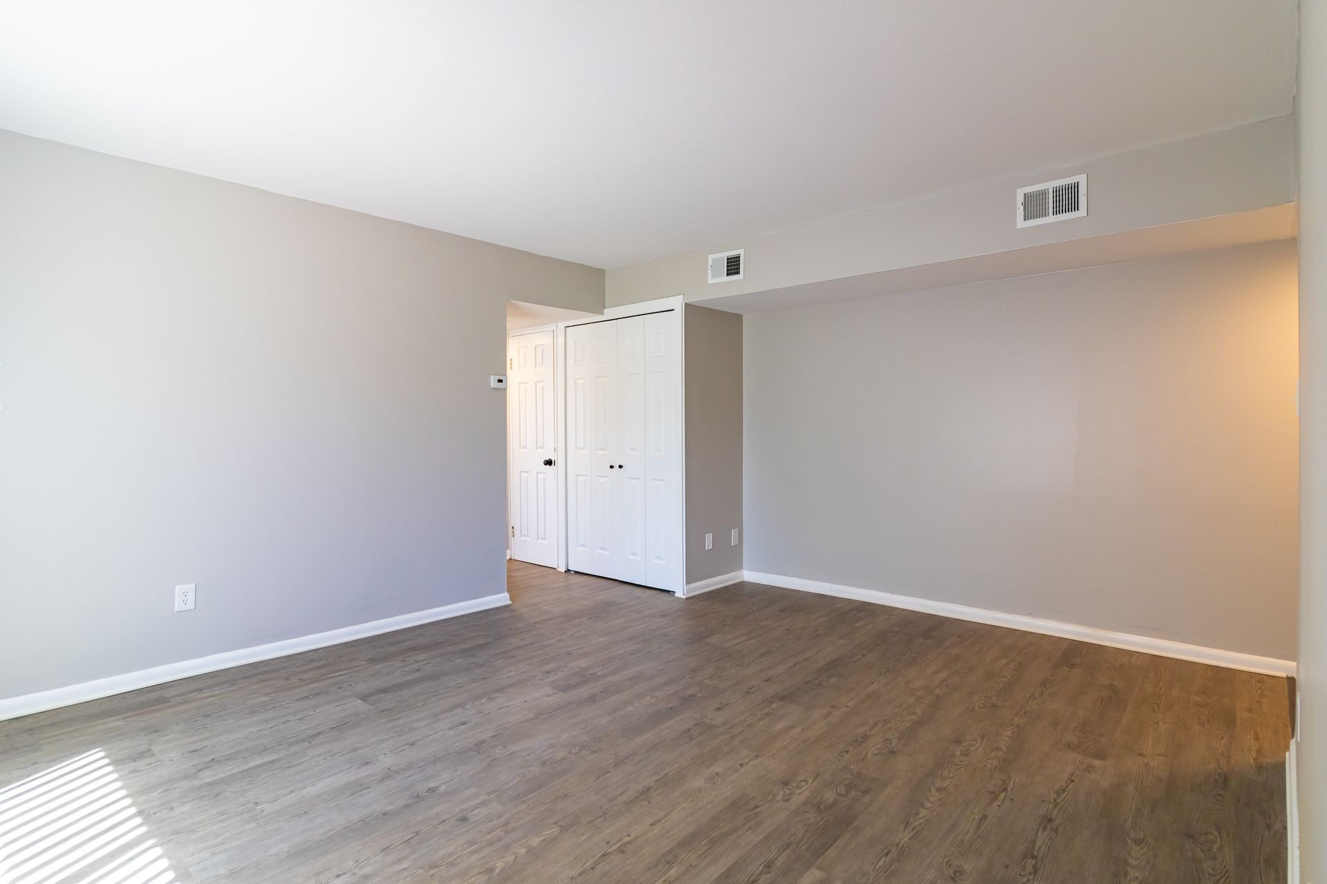 Empty room with gray walls, white closet doors, and wood-look flooring.