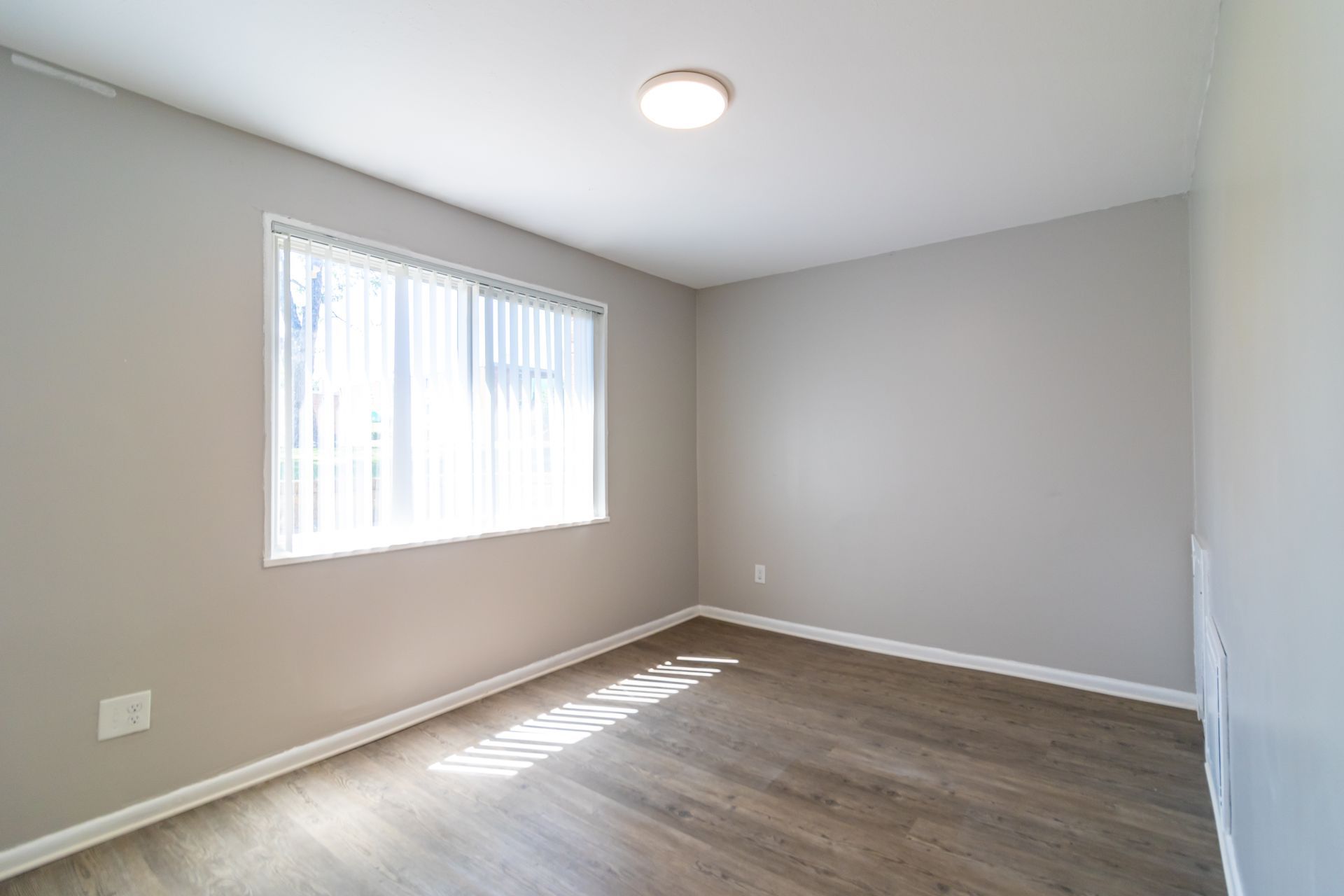 Empty room with gray walls, window with blinds, and wood floor.