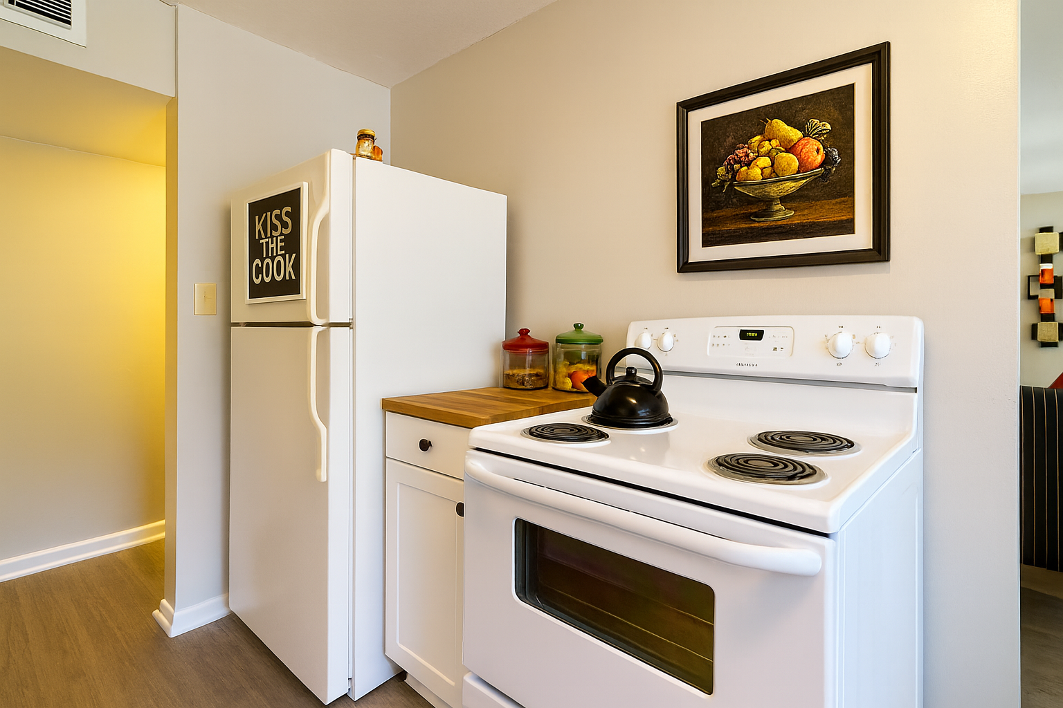 White kitchen with stove, refrigerator, and framed artwork.