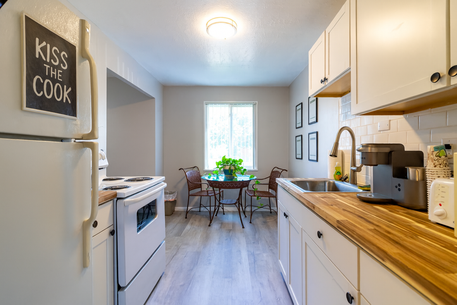 Kitchen with white cabinets, appliances, and wood countertops; small table and chairs.