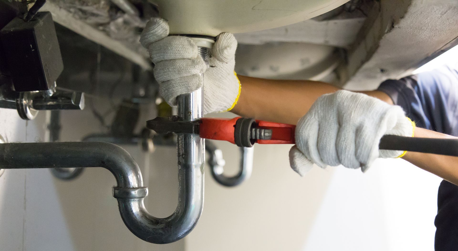 a plumber is fixing a sink pipe with a wrench .