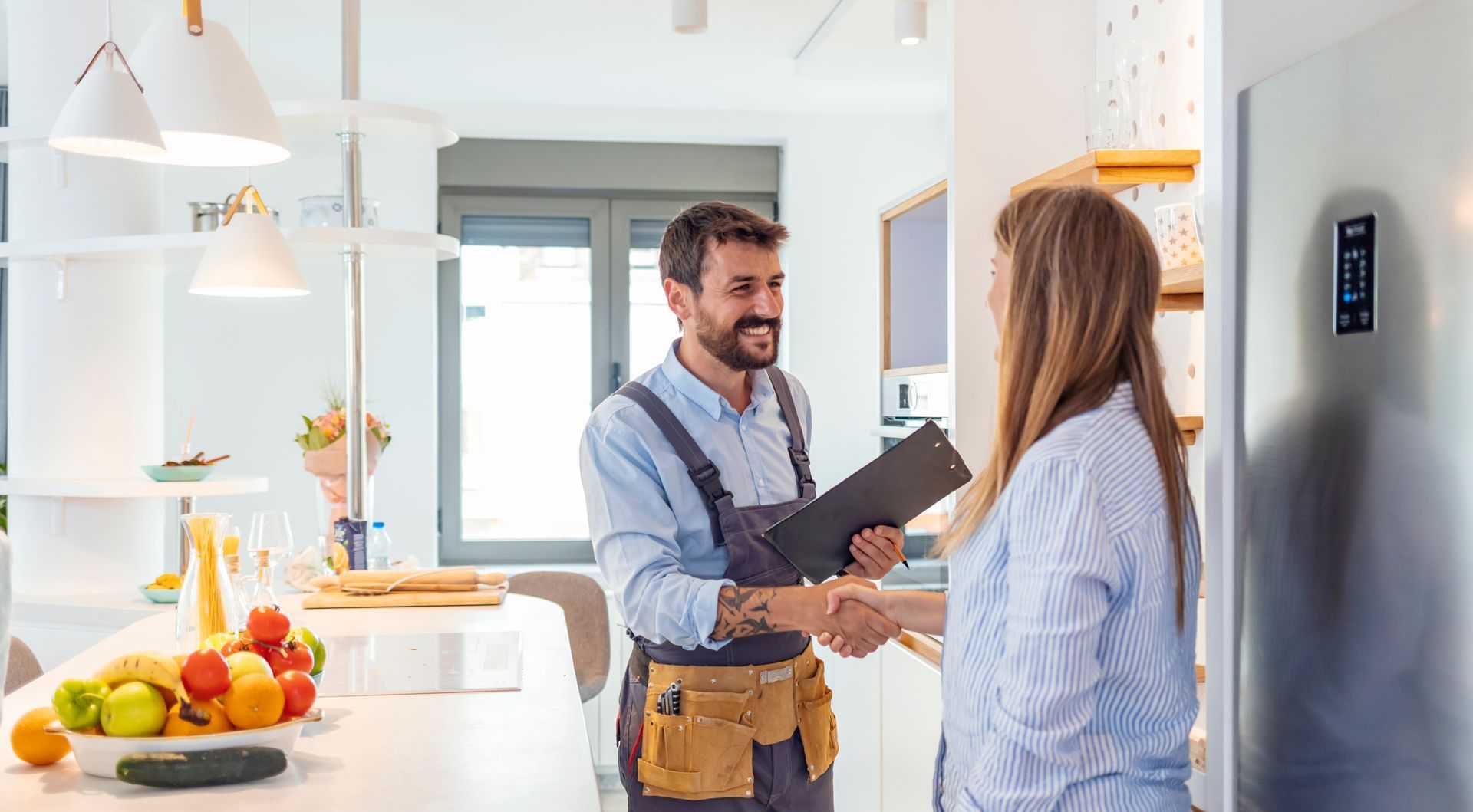 a man is shaking hands with a woman in a kitchen while holding a clipboard .