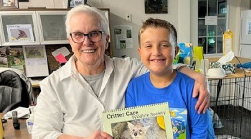 Woman in glasses and boy with a book pose for photo indoors.
