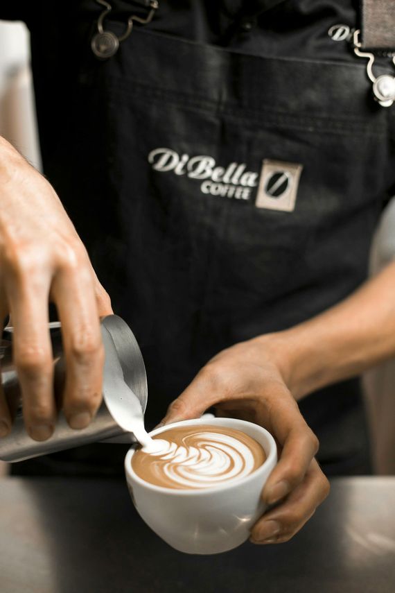 A person in an apron is pouring milk into a cup of coffee