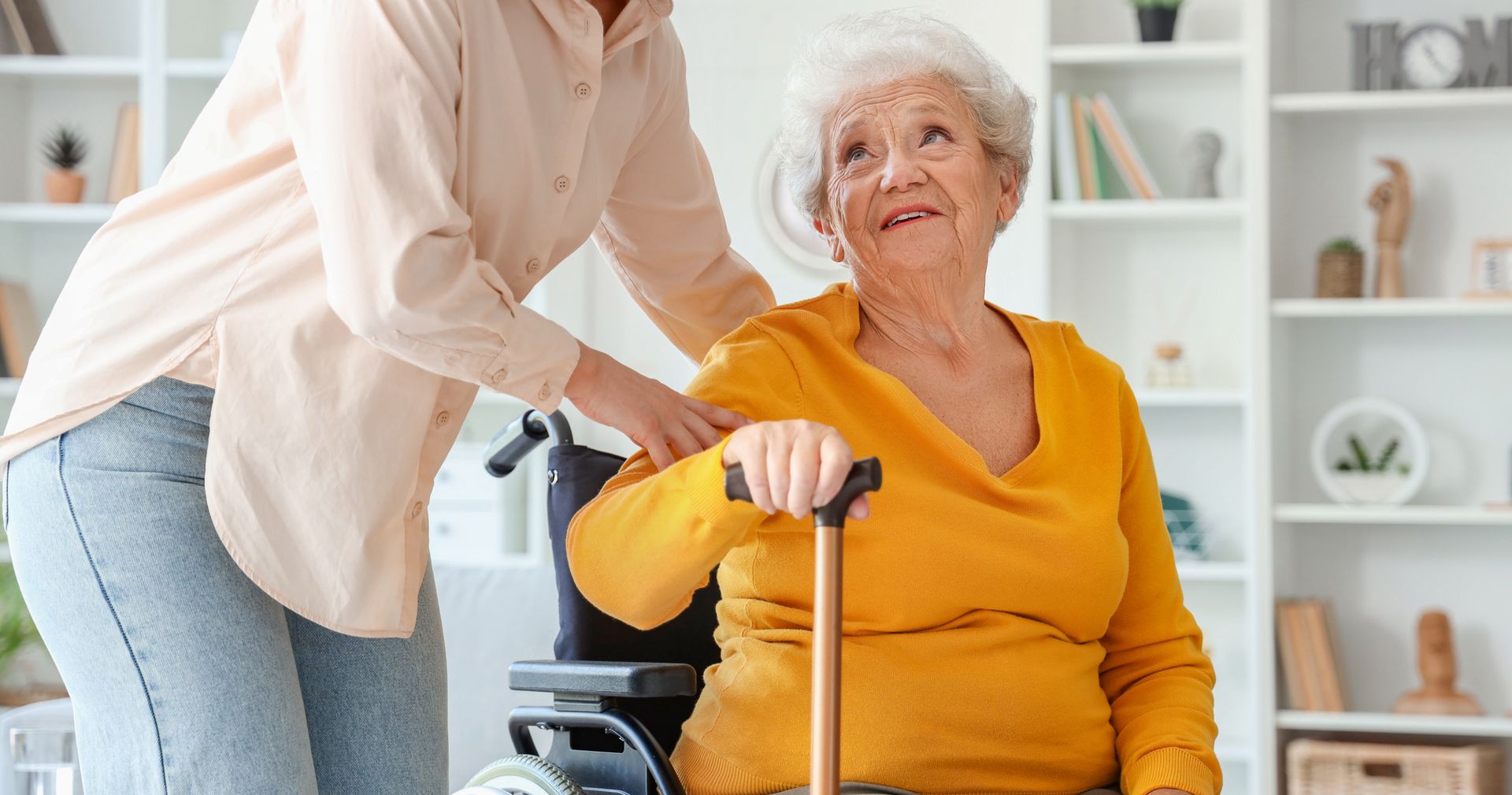 Caregiver assisting an elderly person seated in a wheelchair inside a home Caregiver assisting an elderly person seated in a wheelchair inside a home